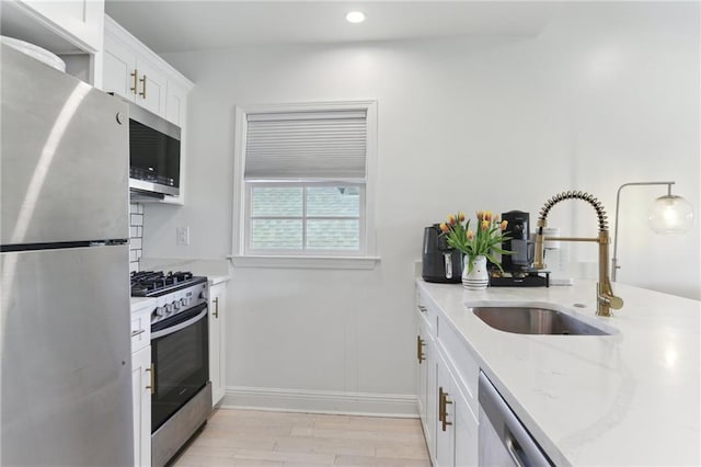 kitchen with light stone countertops, light wood-style flooring, white cabinets, appliances with stainless steel finishes, and a sink