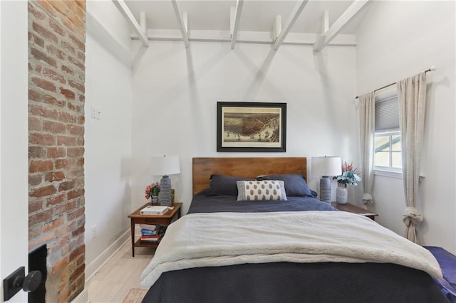 bedroom featuring light wood-type flooring, brick wall, and baseboards