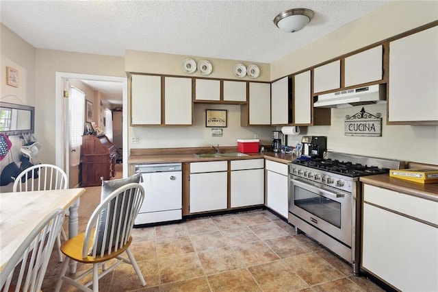 kitchen featuring white dishwasher, a sink, dark countertops, under cabinet range hood, and stainless steel gas range oven