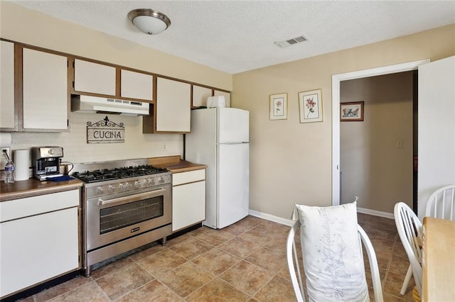kitchen featuring a textured ceiling, freestanding refrigerator, under cabinet range hood, visible vents, and stainless steel range with gas stovetop