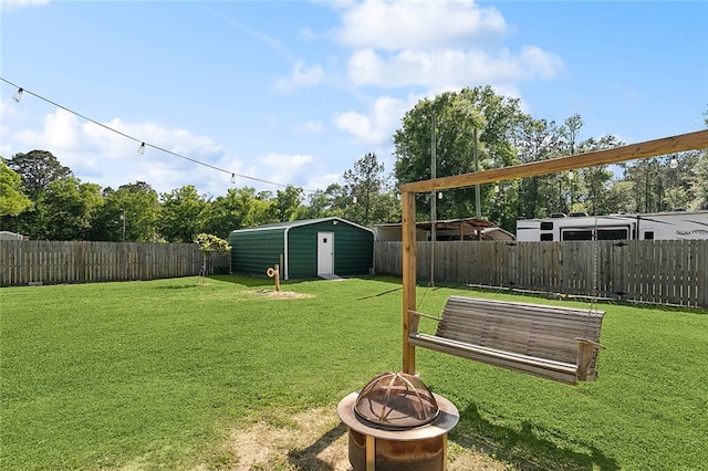 view of yard featuring a storage shed, an outbuilding, a fenced backyard, and a fire pit
