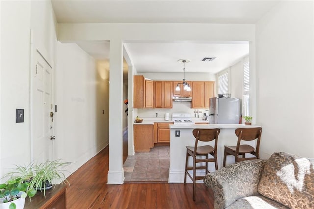 kitchen featuring visible vents, freestanding refrigerator, a kitchen breakfast bar, wood-type flooring, and range