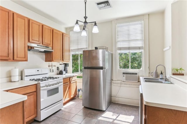 kitchen with white gas stove, freestanding refrigerator, under cabinet range hood, visible vents, and a sink
