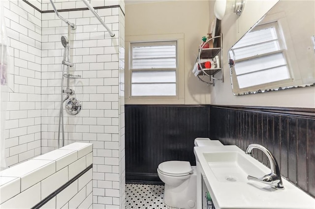 full bath featuring a tile shower, vanity, tile patterned flooring, a wainscoted wall, and toilet