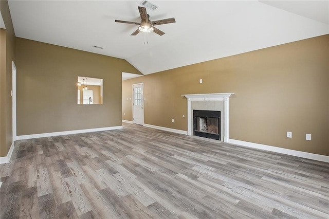 unfurnished living room with a ceiling fan, visible vents, vaulted ceiling, a tile fireplace, and wood finished floors