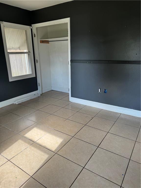 unfurnished bedroom with light tile patterned floors, a closet, and baseboards