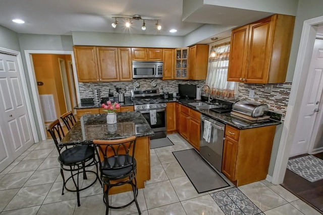 kitchen with a breakfast bar, brown cabinetry, dark stone counters, stainless steel appliances, and a sink
