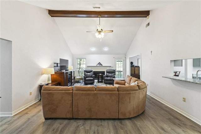 living area featuring baseboards, a ceiling fan, a fireplace, beamed ceiling, and wood finished floors