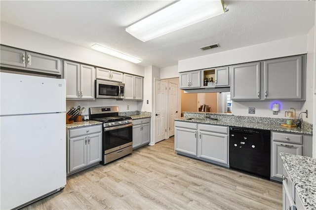 kitchen with gray cabinetry, visible vents, appliances with stainless steel finishes, light wood finished floors, and a sink