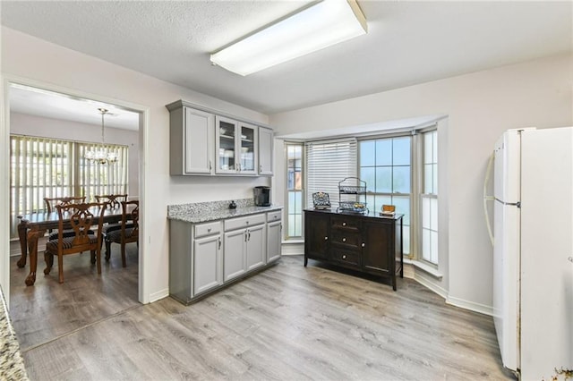 kitchen with glass insert cabinets, an inviting chandelier, freestanding refrigerator, gray cabinetry, and light wood-style flooring