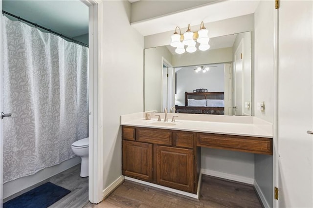 bathroom with vanity, ensuite bath, toilet, wood finished floors, and baseboards