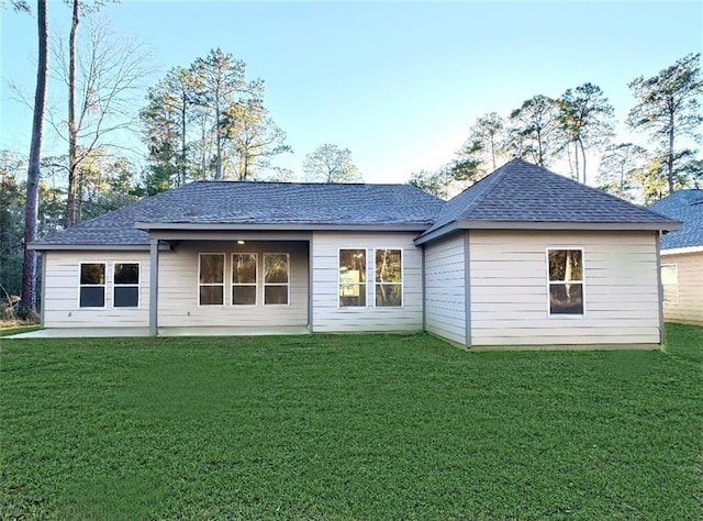 rear view of house with a lawn, a shingled roof, and a patio