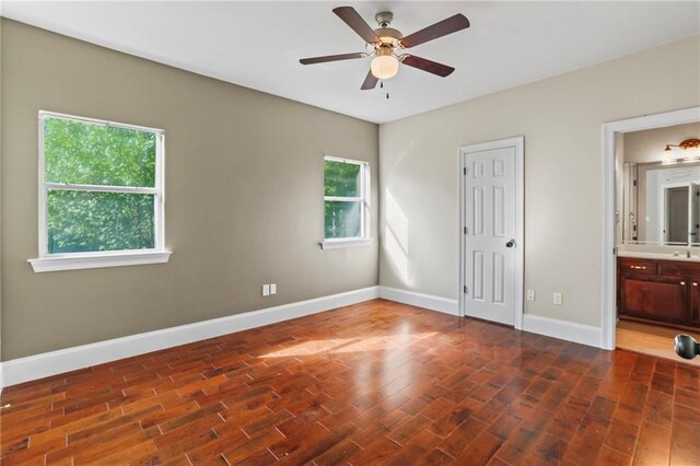 unfurnished bedroom with baseboards, ensuite bath, ceiling fan, a sink, and wood finished floors