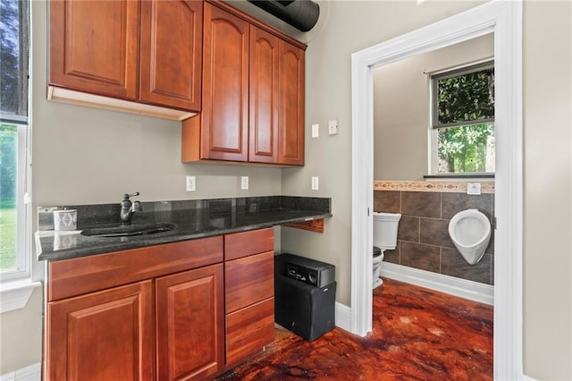 kitchen with a sink, tile walls, a wealth of natural light, and dark stone countertops