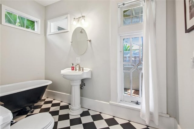 bathroom featuring toilet, tile patterned floors, a soaking tub, and baseboards