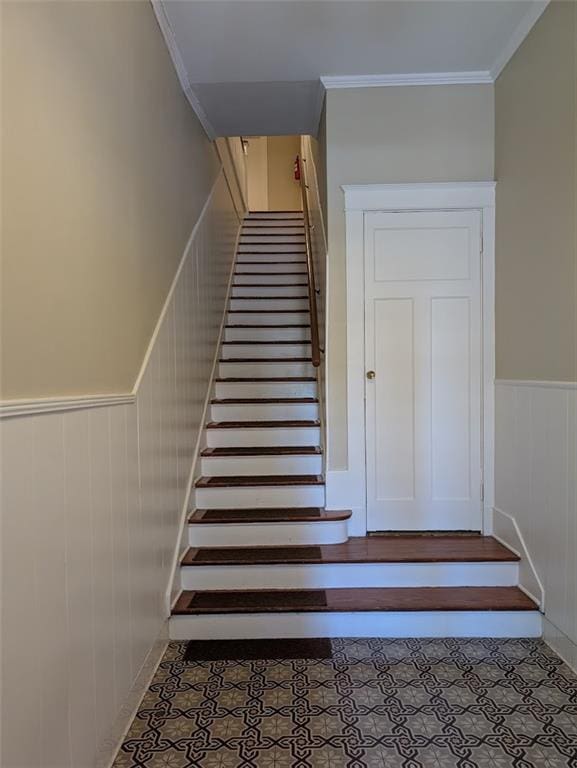 stairway with tile patterned flooring, ornamental molding, and a wainscoted wall