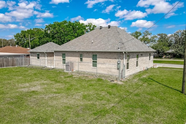 rear view of property with cooling unit, brick siding, a yard, fence, and a shingled roof