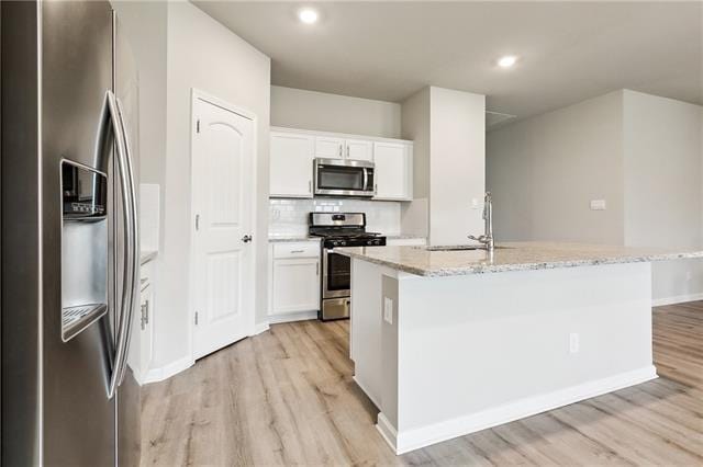 kitchen featuring white cabinets, light stone counters, a sink, light wood-style floors, and stainless steel appliances