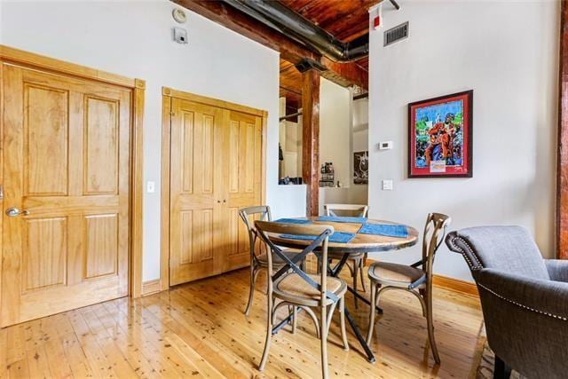 dining area with visible vents, a high ceiling, beam ceiling, and light wood-style flooring