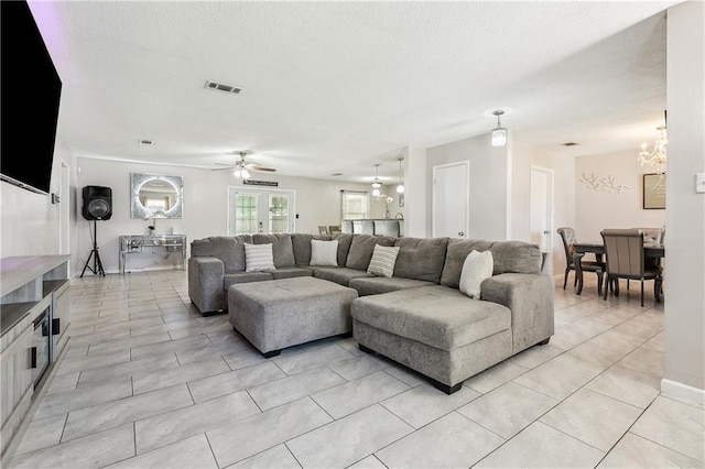 living room with light tile patterned floors, a textured ceiling, visible vents, and ceiling fan with notable chandelier