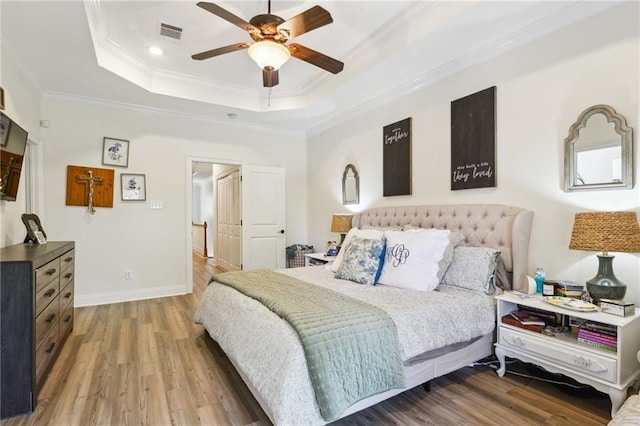 bedroom featuring recessed lighting, crown molding, visible vents, a tray ceiling, and wood finished floors