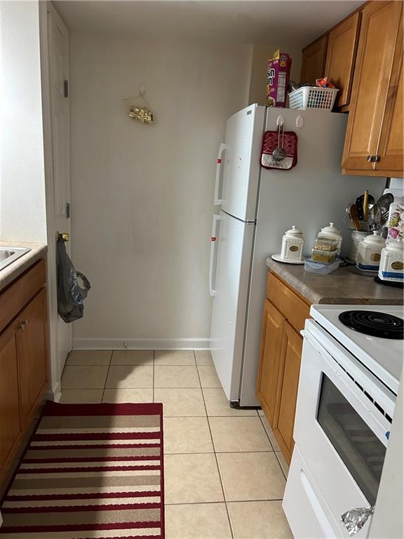 kitchen with white electric range oven, light tile patterned floors, brown cabinetry, and baseboards