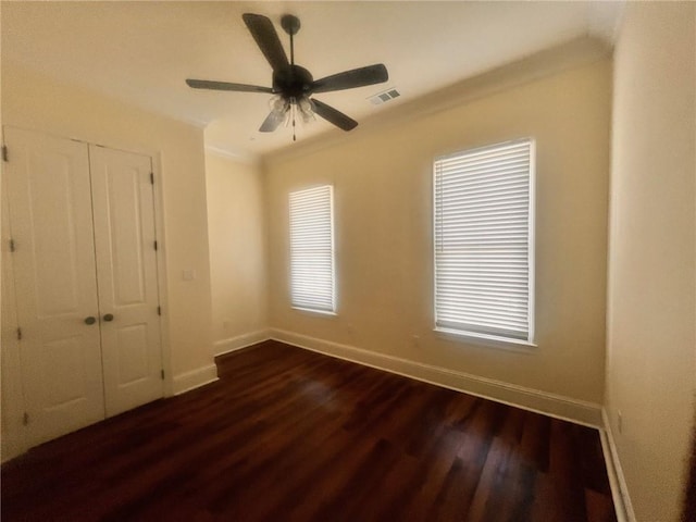 unfurnished bedroom featuring a closet, baseboards, ornamental molding, a ceiling fan, and dark wood-type flooring
