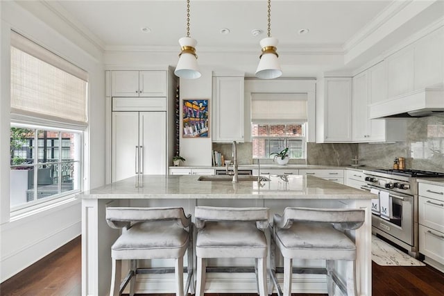 kitchen featuring stainless steel stove, light stone counters, an island with sink, white cabinets, and a sink