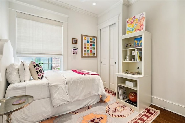 bedroom with wood finished floors, a closet, ornamental molding, and baseboards