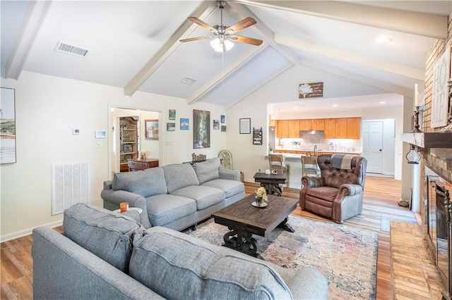 living room with visible vents, light wood finished floors, a fireplace, and a ceiling fan