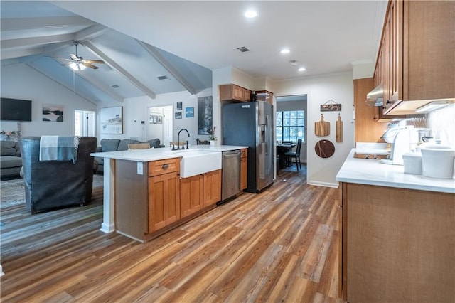 kitchen featuring stainless steel appliances, light wood finished floors, brown cabinetry, and wall chimney range hood