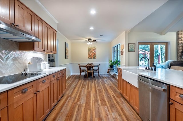 kitchen featuring black electric cooktop, a sink, light countertops, under cabinet range hood, and stainless steel dishwasher
