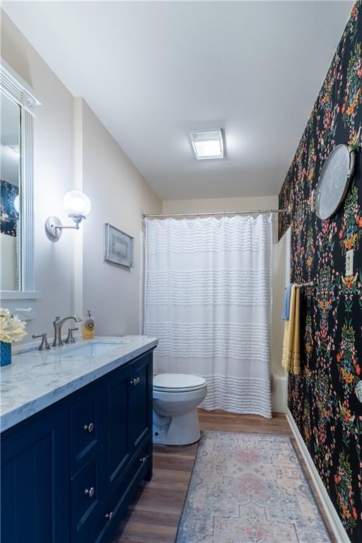 bathroom with toilet, wood finished floors, vanity, and a shower with curtain