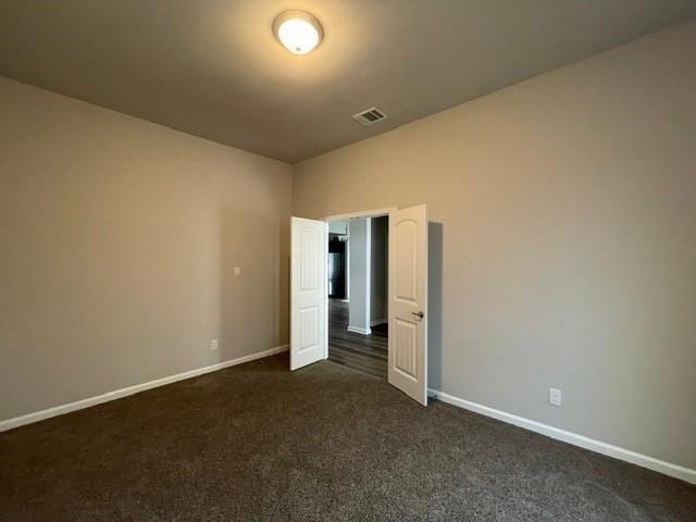 unfurnished bedroom with visible vents, dark carpet, and baseboards