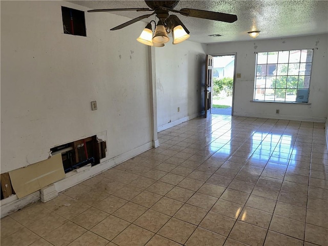 spare room with light tile patterned floors, ceiling fan, baseboards, and a textured ceiling