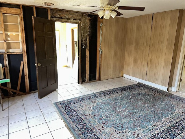 unfurnished room featuring wooden walls, light tile patterned floors, and a ceiling fan