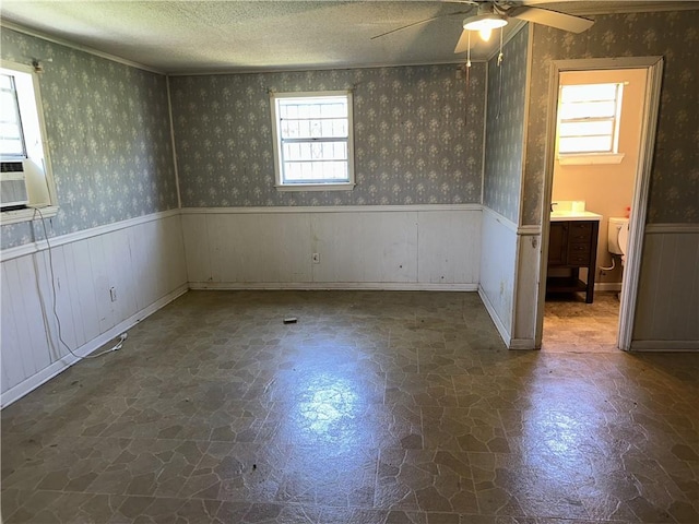 interior space with wallpapered walls, a wainscoted wall, and ceiling fan