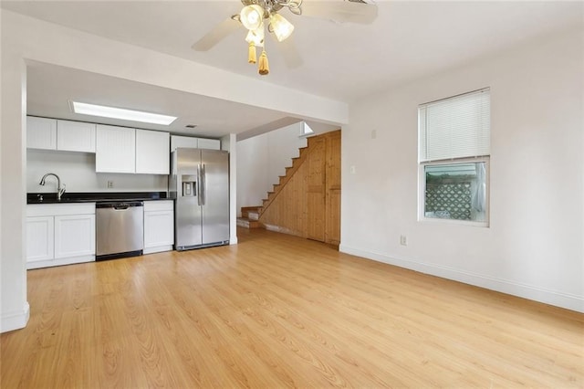 unfurnished living room with baseboards, a sink, ceiling fan, stairway, and light wood finished floors