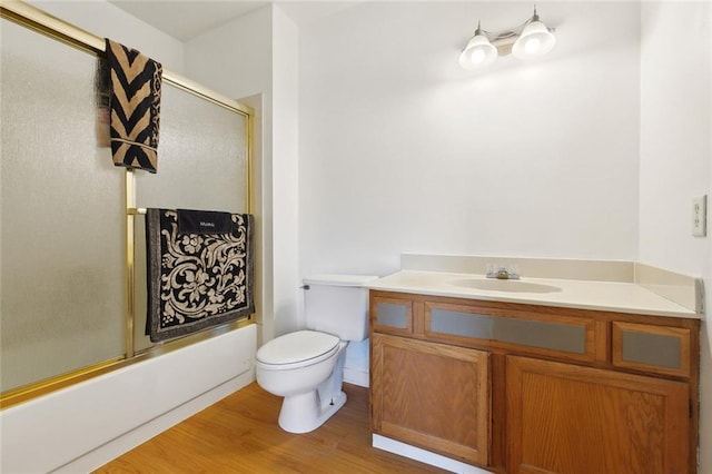 bathroom featuring toilet, wood finished floors, vanity, and bath / shower combo with glass door