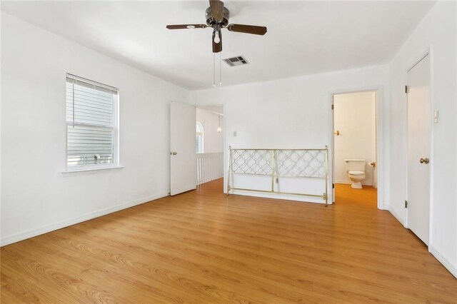 unfurnished bedroom with connected bathroom, light wood-type flooring, a ceiling fan, visible vents, and baseboards