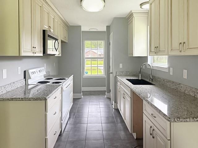kitchen featuring light stone counters, stainless steel microwave, a sink, white electric stove, and baseboards