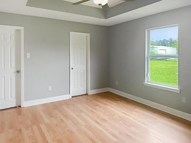spare room with a raised ceiling, light wood-type flooring, baseboards, and ceiling fan