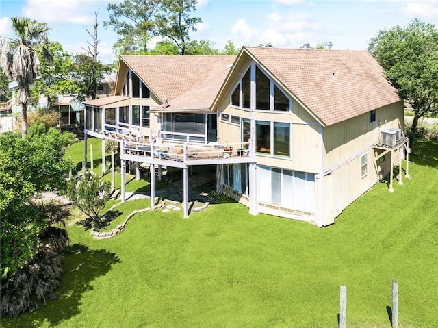 rear view of property featuring a lawn, a wooden deck, a shingled roof, and a sunroom