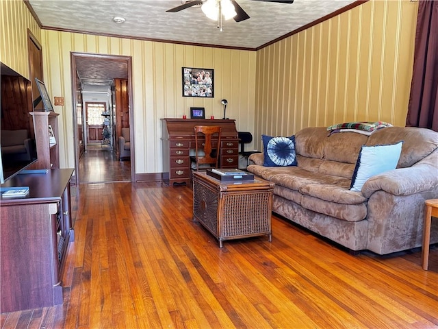 living area featuring crown molding, wood-type flooring, and ceiling fan