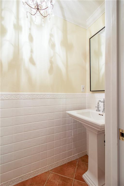 bathroom featuring ornamental molding, a chandelier, tile patterned floors, a wainscoted wall, and tile walls