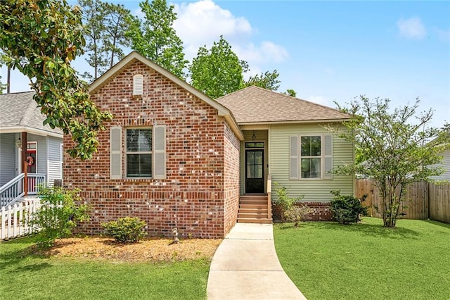 view of front of home featuring brick siding, roof with shingles, a front yard, and fence