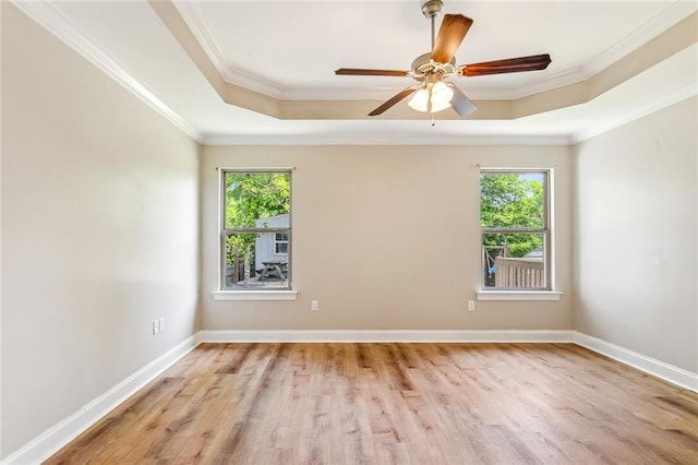 unfurnished room featuring ornamental molding, wood finished floors, a raised ceiling, and a healthy amount of sunlight