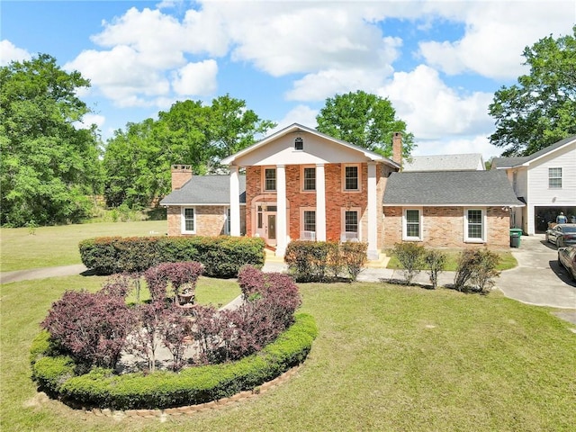 neoclassical / greek revival house with a chimney, a front lawn, brick siding, and concrete driveway