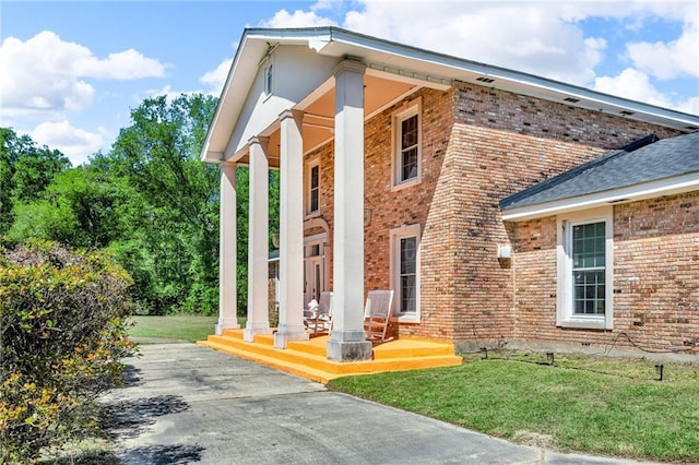 view of property exterior with a porch, a lawn, and brick siding