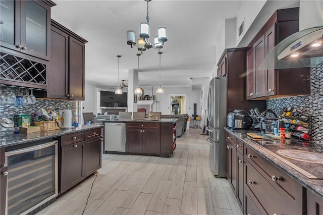 kitchen with stainless steel appliances, decorative backsplash, wall chimney range hood, decorative light fixtures, and beverage cooler
